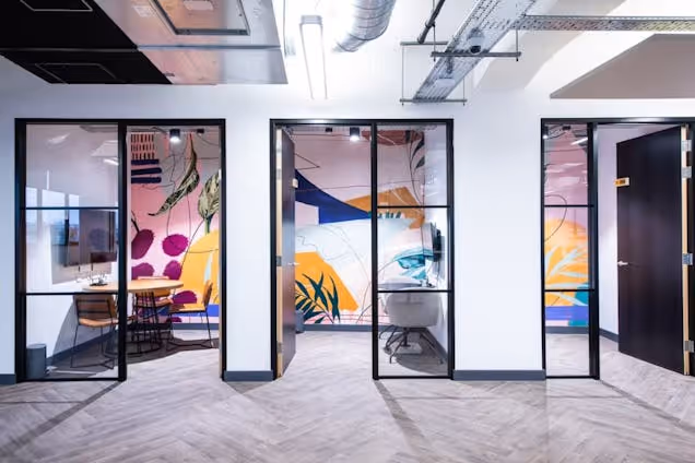 A hallway in an office leads to meeting rooms and phone booths with glass doors and murals on the walls.