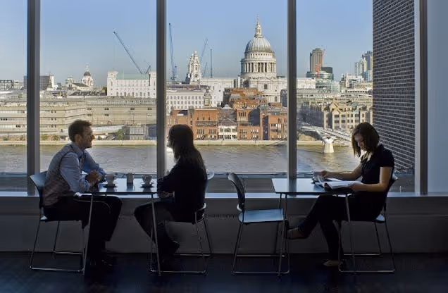 People sat at a table by a window overlooking city buildings and a cathedral dome.