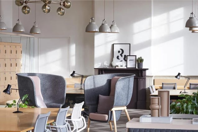 High-back chairs and wood desks with lamps in an office breakout space with pendant lights and a fireplace.