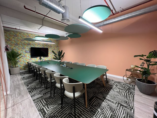 Chairs surround a dark green table in a room with a pink wall, a screen, and a patterned rug on the floor.