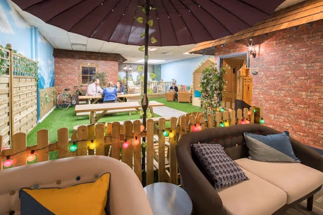 Cosy lounge with sofas, brick walls and warm lighting overlooking a playful mini golf-style setup with greenery.
