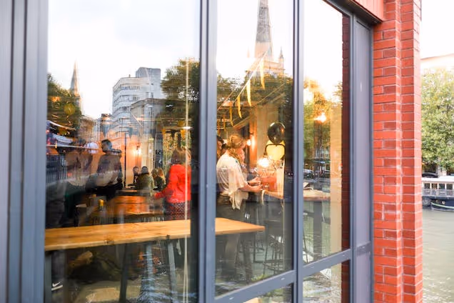 People socialising inside a café, seen through large glass windows with reflections of the street outside.