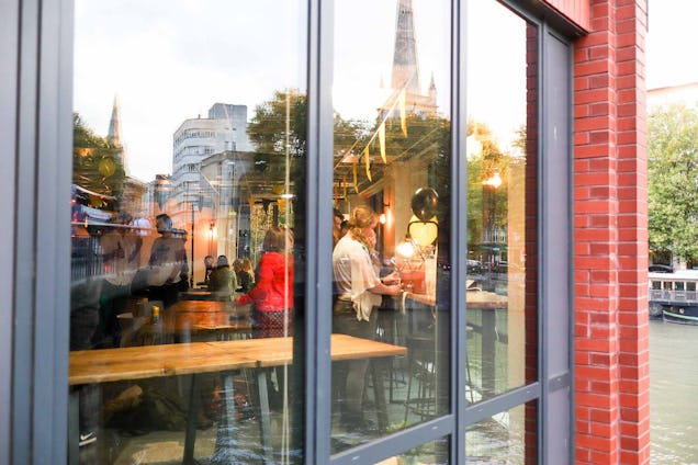 People socialising inside a café, seen through large glass windows with reflections of the street outside.