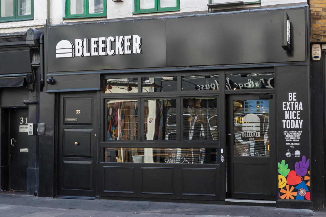 The black exterior of a burger restaurant sits on a city street with a sign above the door.