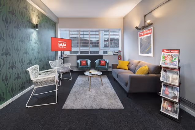 Lounge area with sofas, chairs and a rug, featuring screens and a brochure stand in a cosy workspace.
