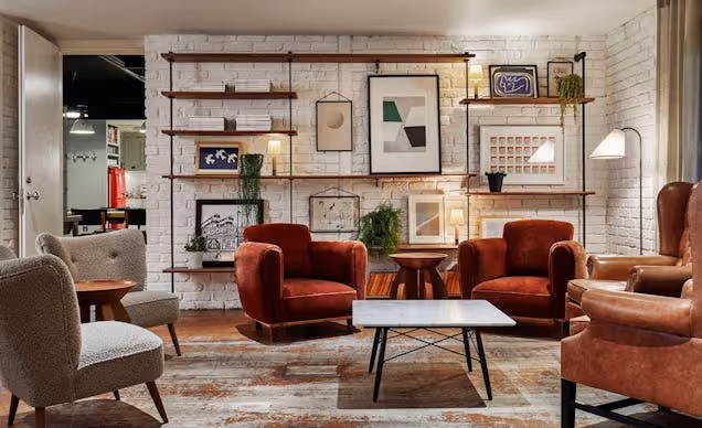 Cosy lounge with armchairs, sofa, coffee table and wall art, styled with warm tones and soft lighting.