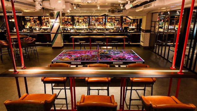 Stylish bar interior with high stools, a long counter and a central illuminated feature, set in a modern venue.