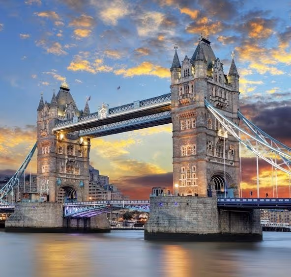 Tower Bridge in London at sunset, with illuminated towers and reflections on the River Thames.