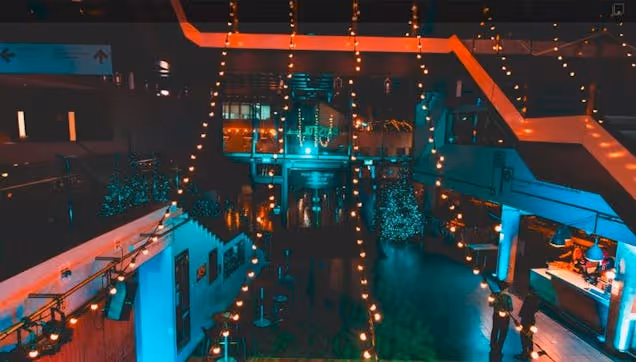 Large indoor venue with colourful lighting, string lights and multiple levels, set up for an evening event or gathering.
