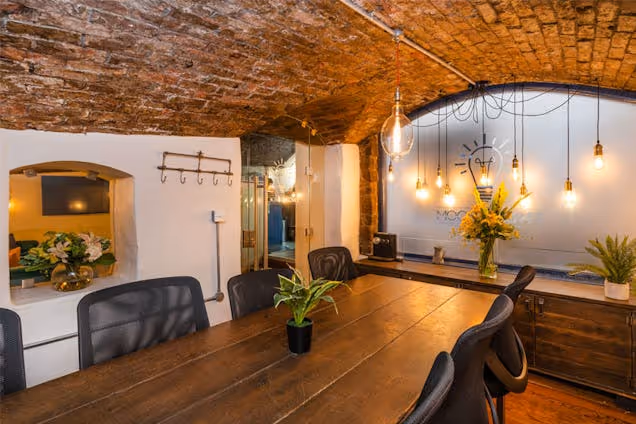 Meeting room with a long wooden table, exposed brick ceiling, glass partition and warm pendant lighting.