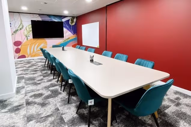 Vibrant boardroom with a long white table, teal velvet chairs, a deep red accent wall, and a colourful botanical mural.
