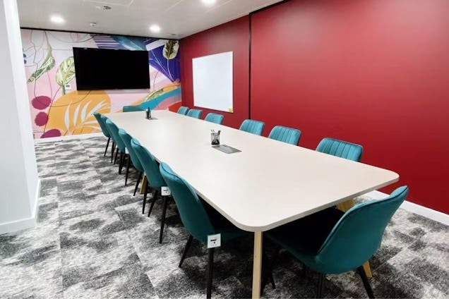 Vibrant boardroom with a long white table, teal velvet chairs, a deep red accent wall, and a colourful botanical mural.
