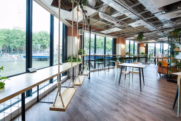 Office breakroom featuring wooden swing seats at a window counter overlooking a river and lush green trees.