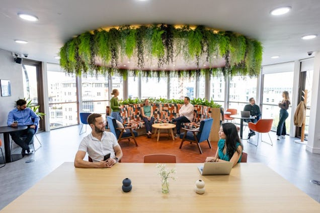 Coworking hub with a large circular ceiling planter, blue armchairs, and professionals working in a bright, open-plan space.