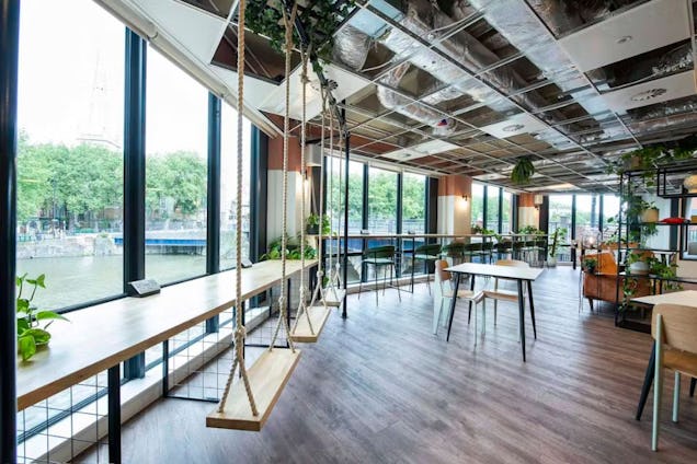 Riverside office featuring a long window-side counter with wooden swings for seats and an industrial-style exposed ceiling.
