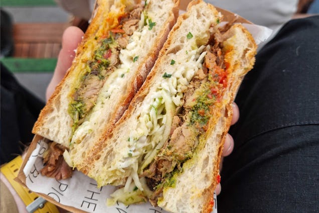 Close-up of a large sandwich filled with shredded vegetables and sauce, held in hands over a takeaway wrapper.