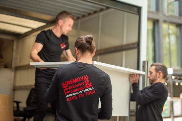 The Removal & Delivery Company Staff in black uniforms carefully load a large white piece of furniture into the back of a moving van.