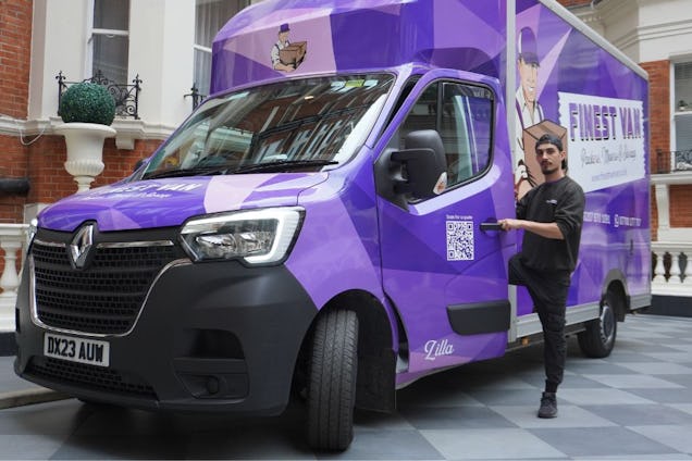 A purple Finest Van removal truck parked on a tiled driveway in front of a residential building. There is a man in the Finest Van uniform getting into the truck.