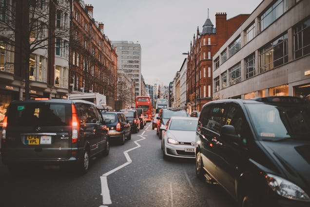 A busy London street filled with traffic, featuring black taxis and cars lined up between historic brick buildings.