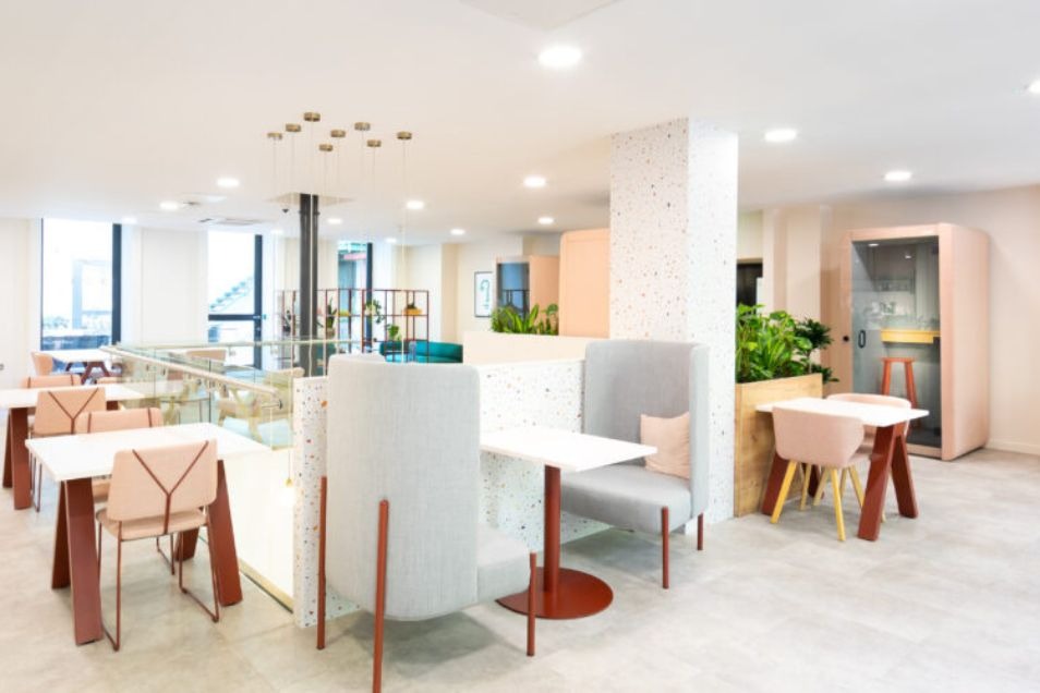 Modern office with high-back booths, light pink seating, and a private phone pod surrounded by indoor greenery.