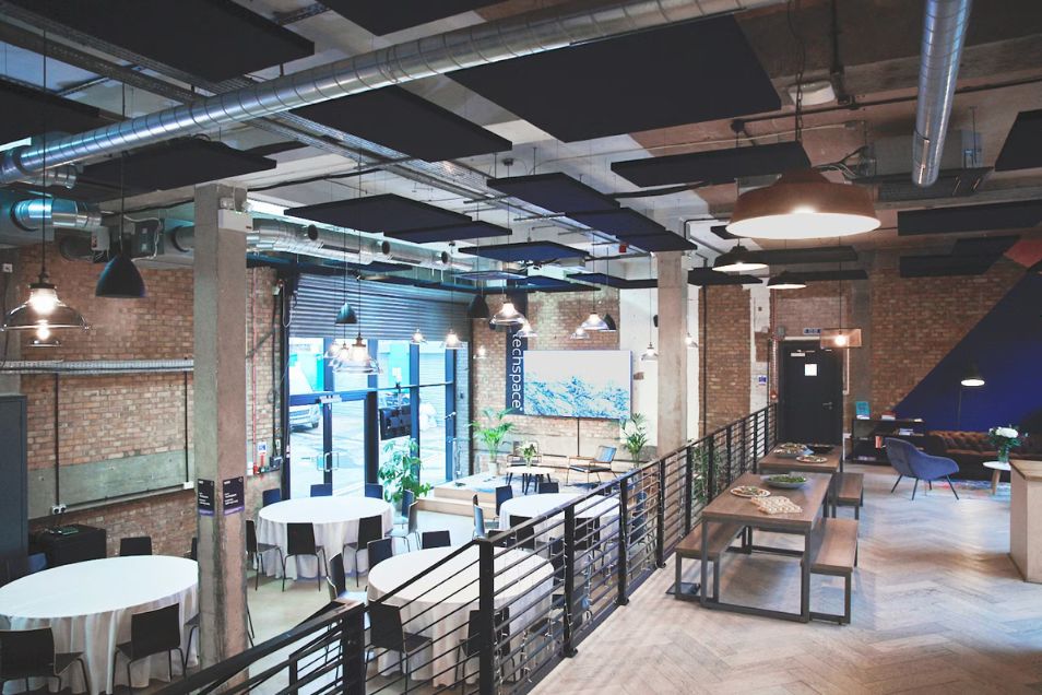 Tables and benches are arranged in an office event space with brick walls and exposed ceiling pipes.