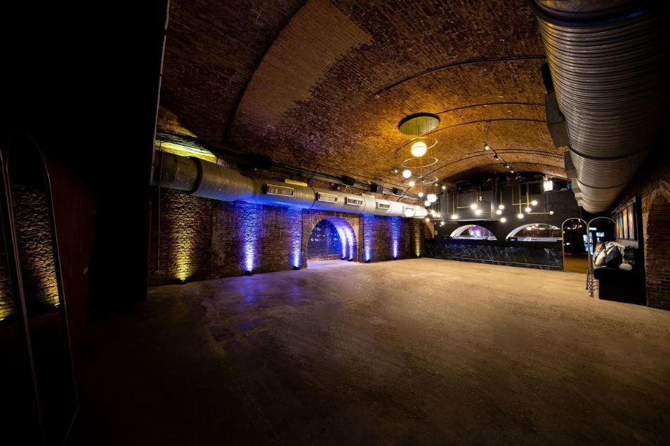 An empty event space located in a brick tunnel with blue floor lighting.