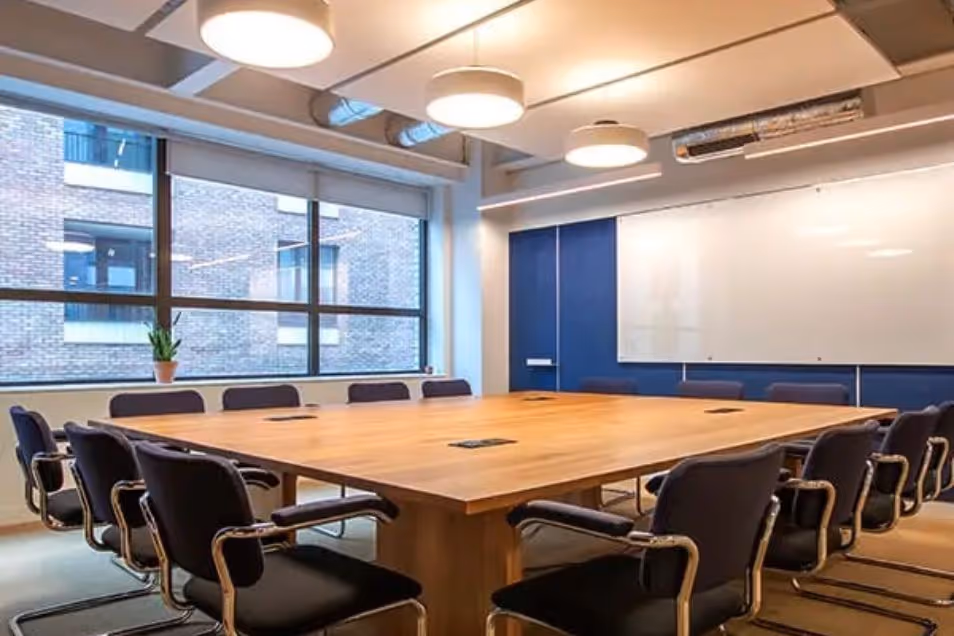 Conference room featuring a large square wooden table, black ergonomic chairs, and floor-to-ceiling windows.
