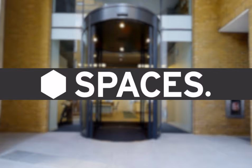 The "SPACES." logo is displayed over a blurred view of a revolving glass door entrance to a building.