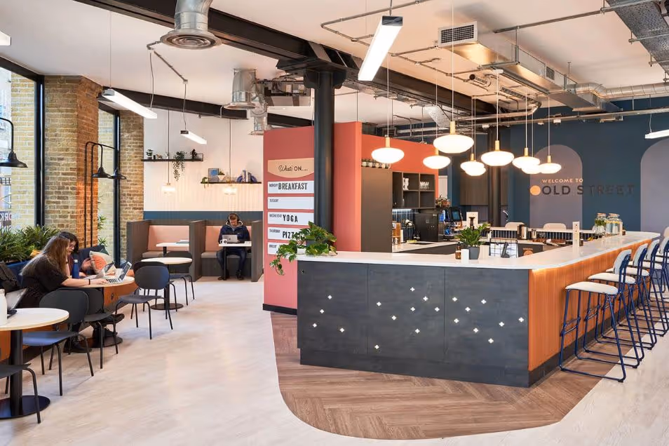 A person working at a cafe table near an office bar with globe lighting and dark wood accents.