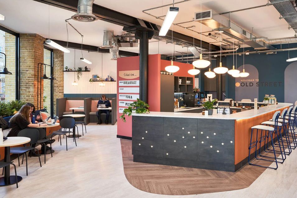 A person working at a cafe table near an office bar with globe lighting and dark wood accents.