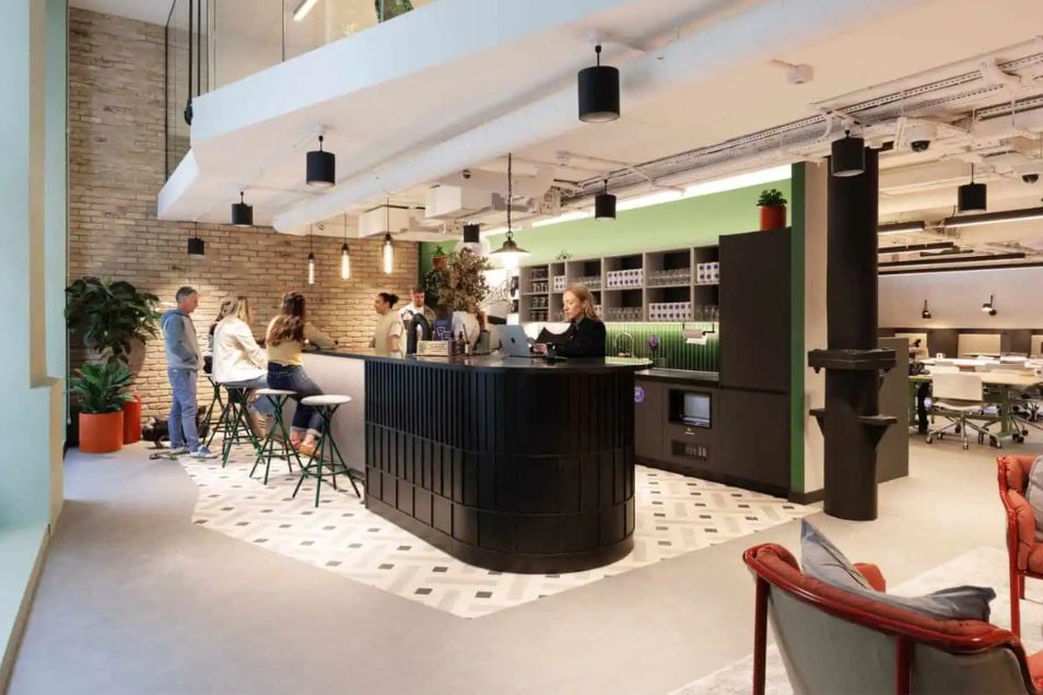 People socialising and sitting at a curved black bar in a stylish office breakout area with exposed brick and industrial lighting.