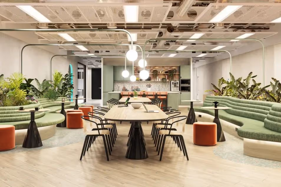 Coworking space with a long communal table, green tiered seating, and lush indoor plants under industrial lighting.