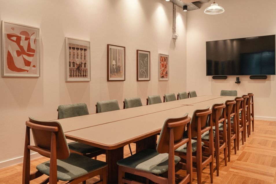 Boardroom with a long wooden table, green upholstered chairs, parquet flooring, and a gallery wall of framed art.
