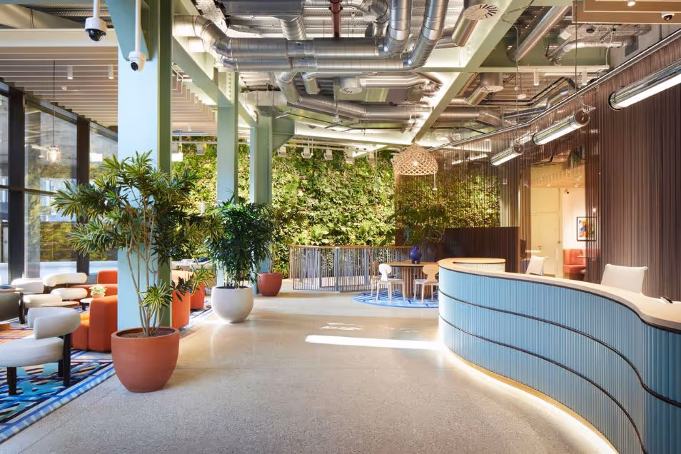 Office reception featuring a curved light-blue desk, a green wall, and exposed ceiling ductwork.