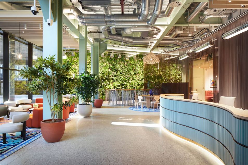 Office reception featuring a curved light-blue desk, a green wall, and exposed ceiling ductwork.