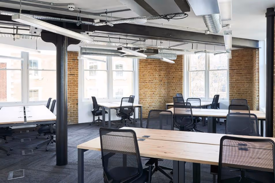 Office featuring exposed brick walls, black structural pillars, and wooden desks with black mesh chairs.