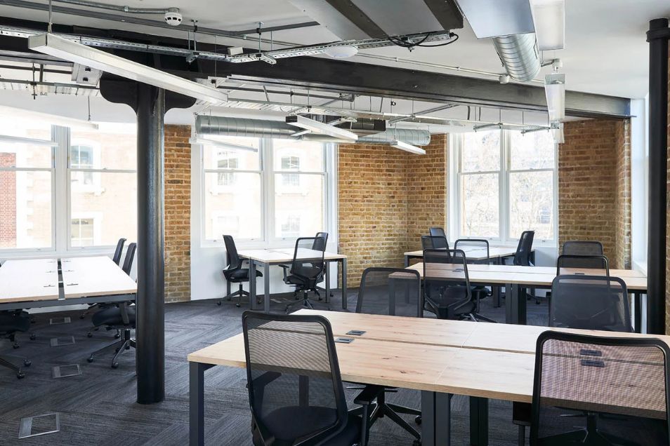 Office featuring exposed brick walls, black structural pillars, and wooden desks with black mesh chairs.