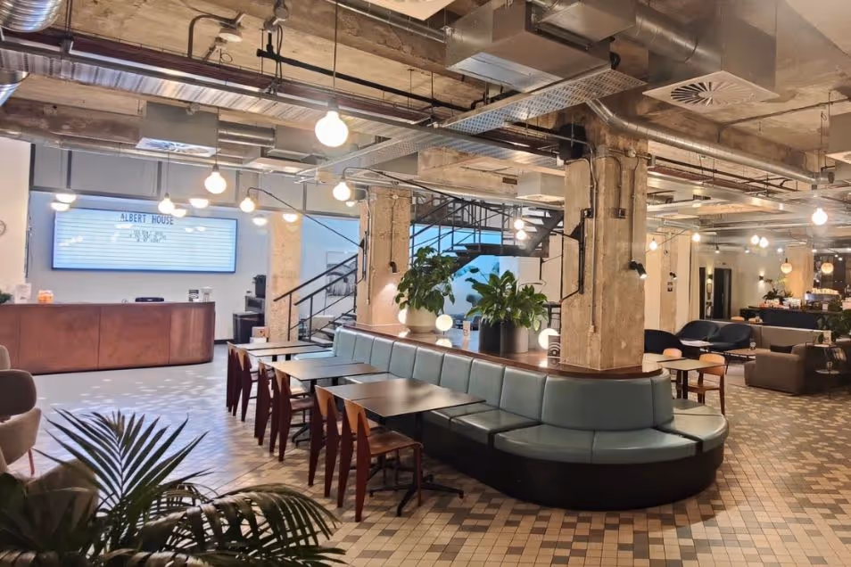 Lounge with a teal banquette and patterned tile floors. There is a pink wooden reception desk with hanging lights dangling from the ceiling.