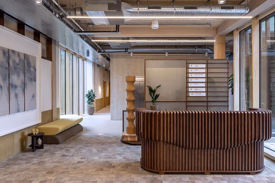 Office reception area with a curved dark-wood slat desk, light stone flooring, and warm ceiling lighting.