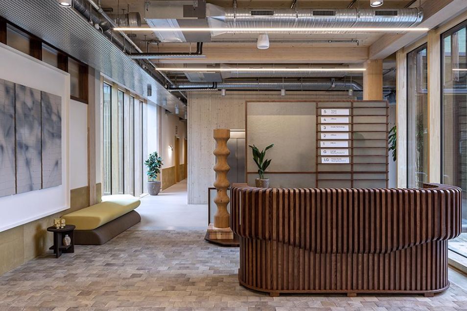 Office reception area with a curved dark-wood slat desk, light stone flooring, and warm ceiling lighting.