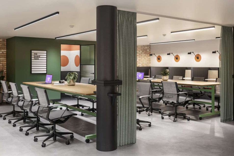Long tables with black chairs in an office space featuring green walls and a pillar.