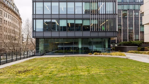 An office building with glass windows stands behind a patch of grass and a walkway.