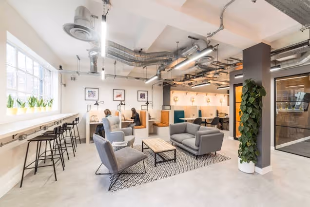 Armchairs and a sofa on a rug in an office lounge near a counter with stools.
