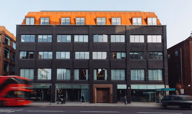 A bus and a car drive past a five-story building with a copper-colored roof on a city street.
