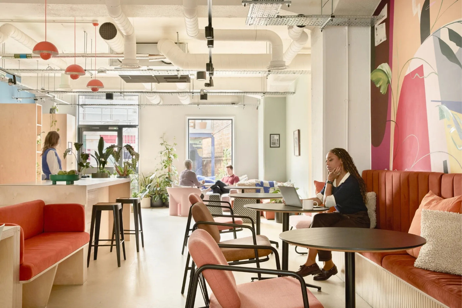 People sat at tables working on laptops in an office communal space with booth seating and a mural.