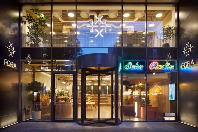 A building entrance at night features a revolving glass door, windows, and "FORA" signs.
