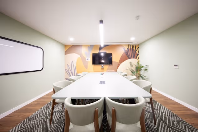 A white table with chairs in a meeting room featuring a whiteboard and patterned rug.
