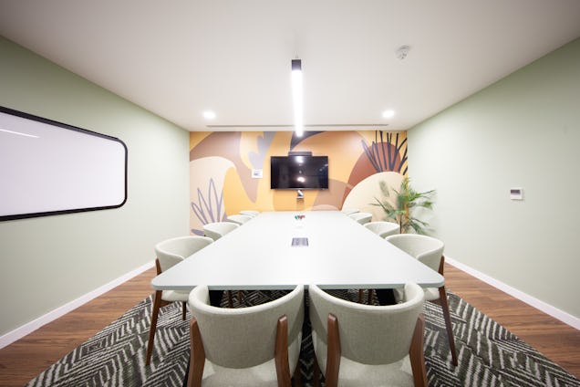A white table with chairs in a meeting room featuring a whiteboard and patterned rug.