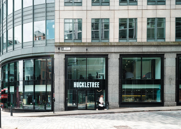 A stone building features large ground-floor windows with "HUCKLETREE" signage and a person visible inside.