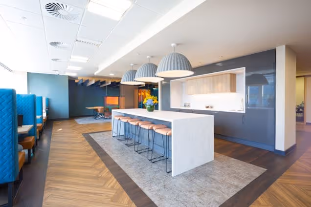 A kitchen island with bar stools in a co-working space featuring wood floors and pendant lights.